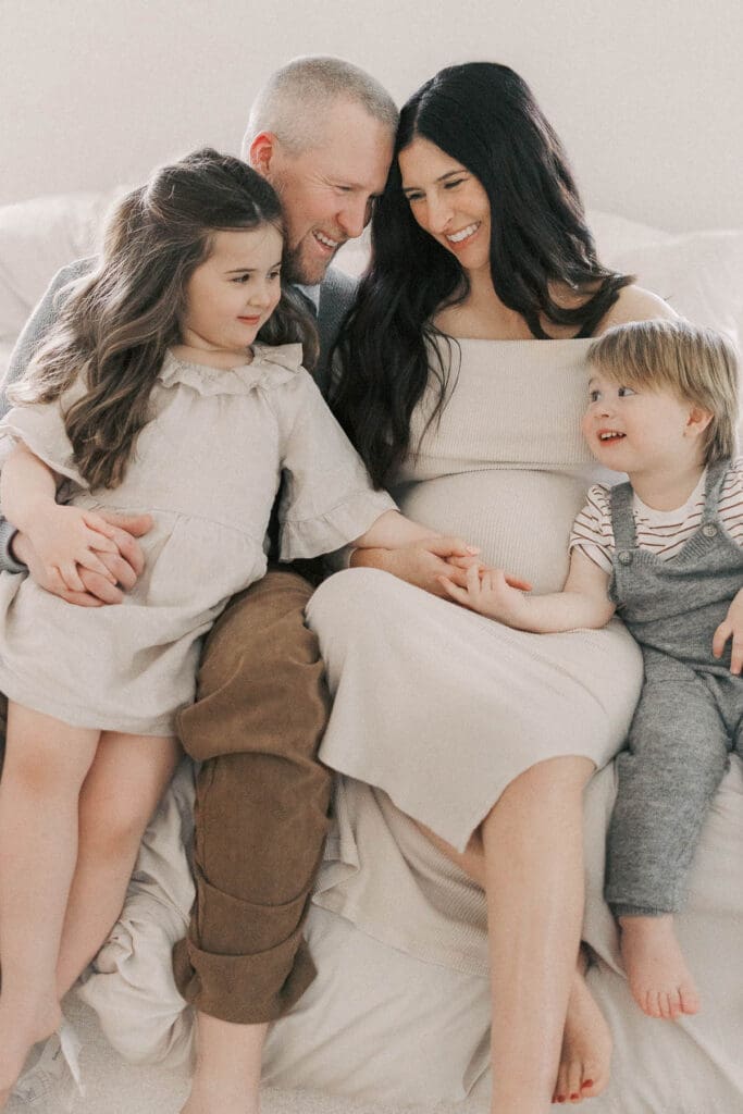 Father holding his young daughter while standing beside expectant mother holding their son during cozy in-home maternity photos in Kansas City.