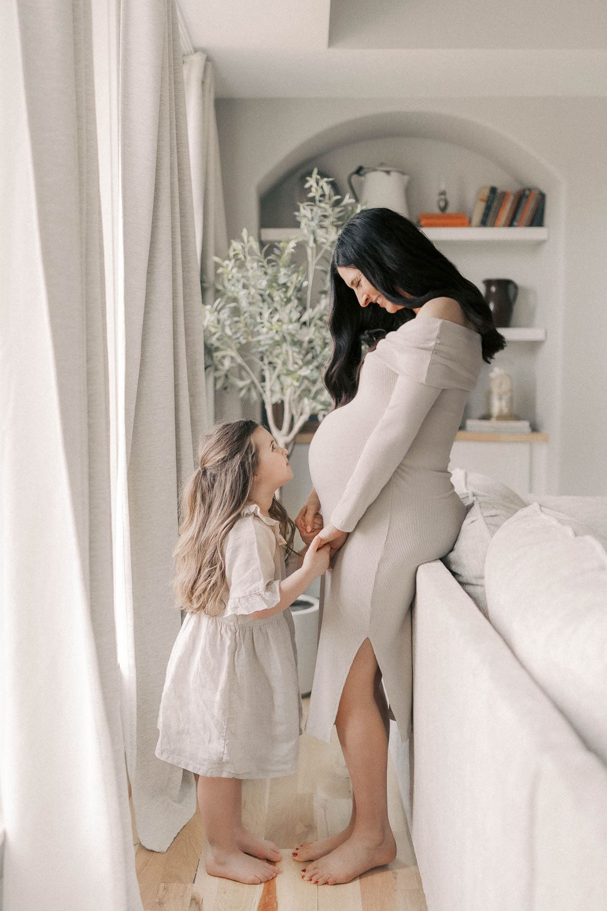 Little girl smiles at ay her mother during in-home maternity photos in Kansas City for a twin pregnancy.